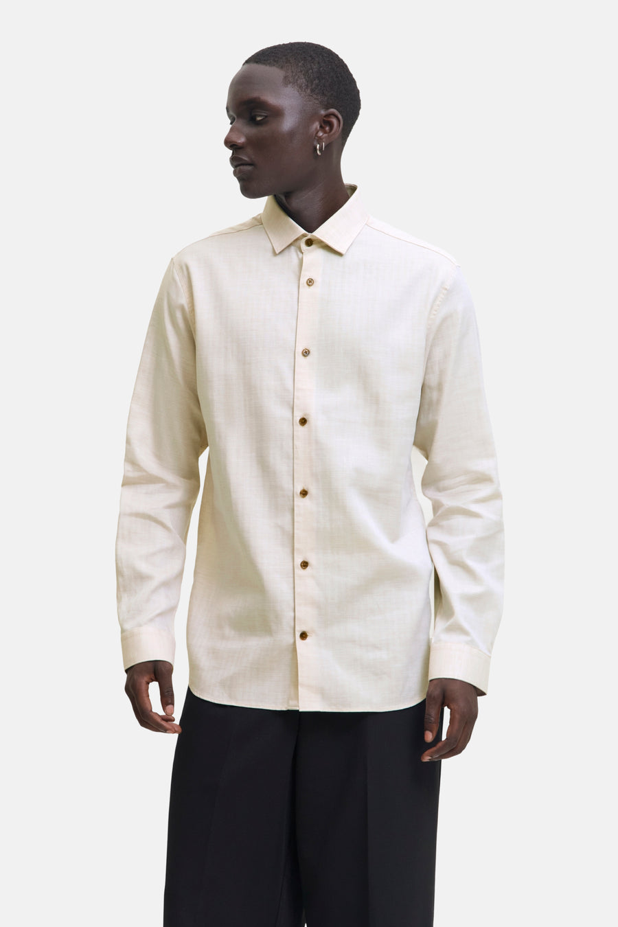 Chemise beige à manches longues de PREMIUM by JACK & JONES, avec boutons marron et portées avec un pantalon noir.