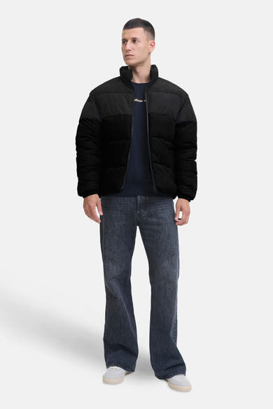 Kort zwart jack van Jack & Jones, gedragen met een marineblauwe trui en een verbleekte spijkerbroek.