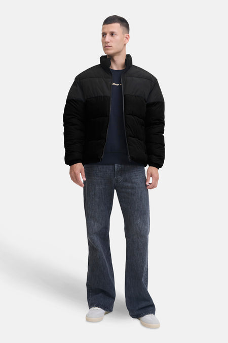 Kort zwart jack van Jack & Jones, gedragen met een marineblauwe trui en een verbleekte spijkerbroek.