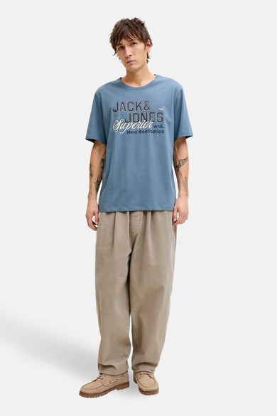 T-shirt à manches courtes bleu d'ORIGINALS BY JACK & JONES, avec un imprimé décoratif sur le devant, porté avec un pantalon beige.