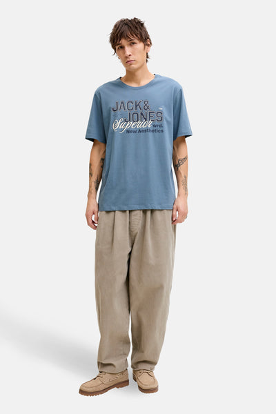 T-shirt à manches courtes bleu d'ORIGINALS BY JACK & JONES, avec un imprimé décoratif sur le devant, porté avec un pantalon beige.