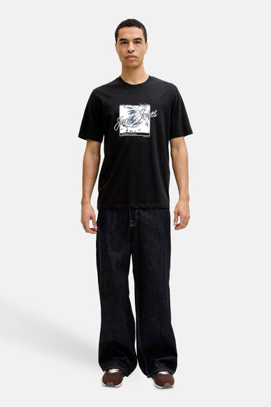 T-shirt à manches courtes noir de JACK & JONES avec un imprimé graphique carré sur le devant, porté avec un jean ample et des chaussures marron.
