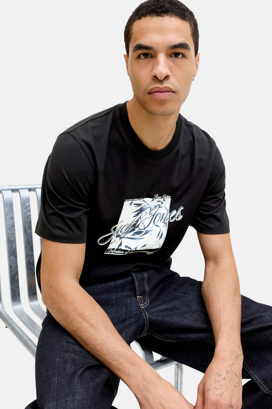 Zwart T-shirt met korte mouwen van JACK & JONES, met een witte grafische print op de voorkant, gedragen met een donkere spijkerbroek.
