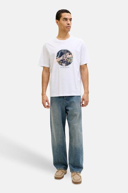 T-shirt à manches courtes blanc de JACK & JONES avec un imprimé tropical, porté avec un jean ample et des chaussures bateau.