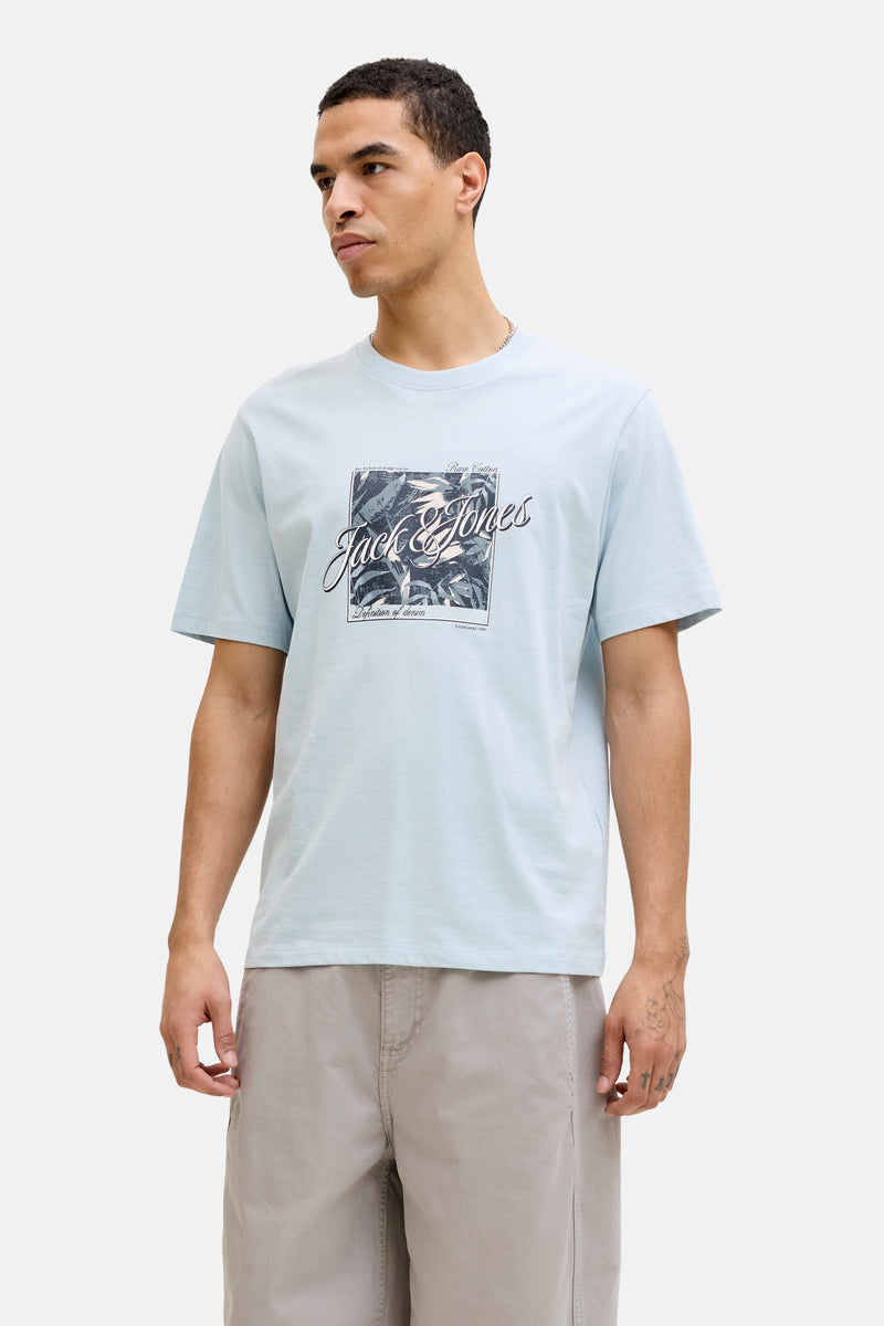T-shirt bleu à manches courtes de JACK & JONES, avec motif graphique imprimé, porté avec un short beige.

