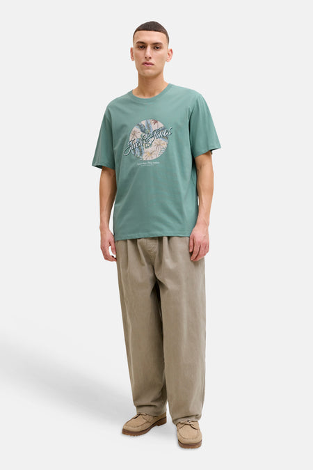 T-shirt bleu à manches courtes de JACK & JONES, avec un imprimé rond centré et porté avec un pantalon ample beige.