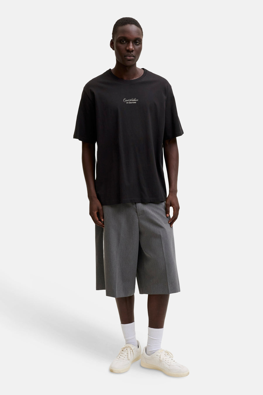 T-shirt noir de ORIGINALS BY JACK & JONES avec l'inscription "Our Archive OF CREATIONS" sur la poitrine, porté avec un short gris et des baskets blanches.
