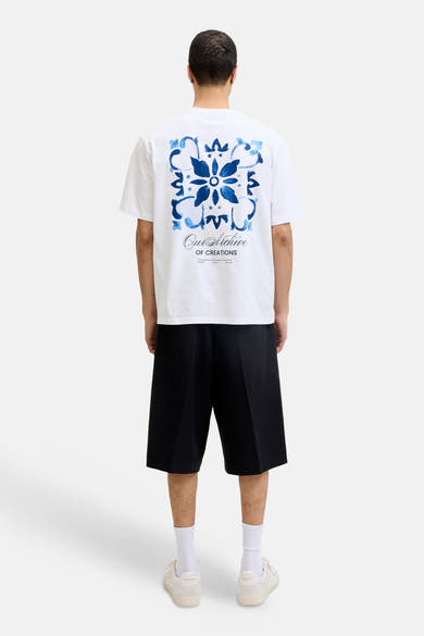 T-shirt blanc de ORIGINALS BY JACK & JONES avec grand motif ornemental bleu et texte au dos, porté avec un short noir.