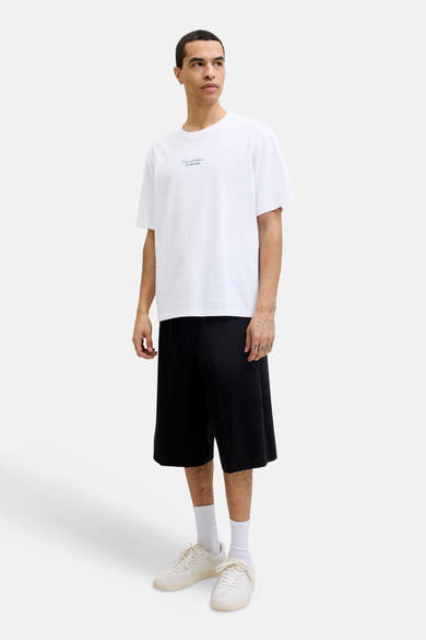 T-shirt blanc de la marque ORIGINALS BY JACK & JONES, avec logo texte discret sur la poitrine, porté avec un short noir et des baskets claires.
