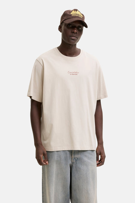 T-shirt beige de ORIGINALS BY JACK & JONES avec texte brodé rouge 'Our Archive' sur la poitrine, porté par un homme.