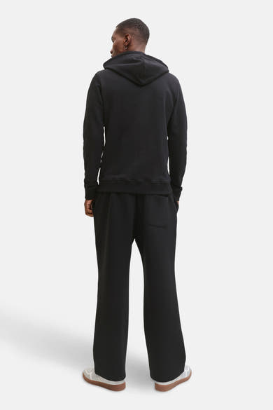 Zwarte hoodie van JACK & JONES, model van achteren gezien met een wijde broek en sportschoenen.