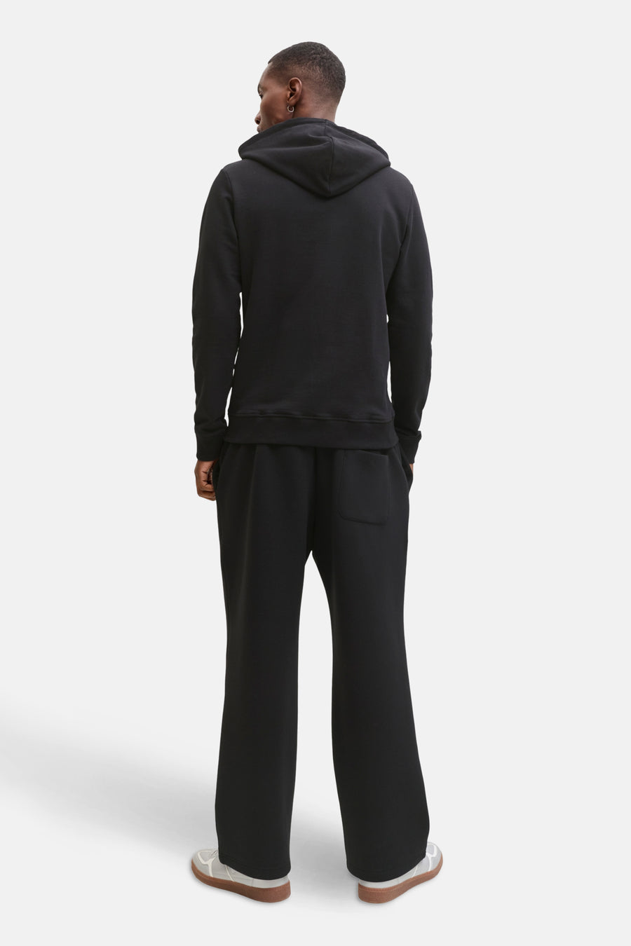 Zwarte hoodie van JACK & JONES, model van achteren gezien met een wijde broek en sportschoenen.