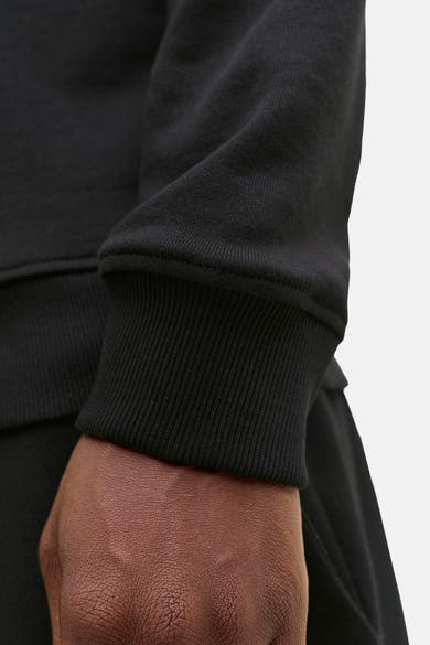 Zwarte sweater van JACK & JONES, met geribde textuur bij de pols, gedragen op gebruinde huid.
