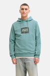 Groene hoodie van JACK & JONES, gedragen met een lichtgewassen spijkerbroek en witte sneakers.