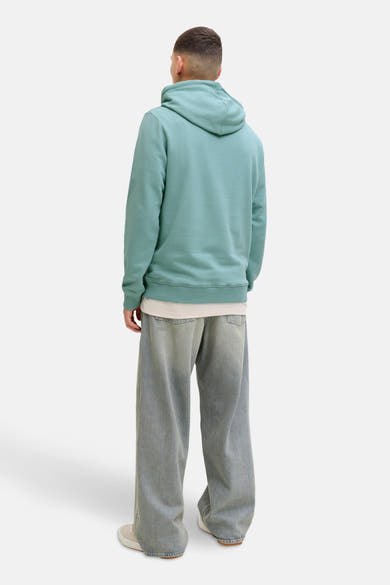 Groene hoodie van JACK & JONES, met capuchon en geribde boorden, gedragen over een wit T-shirt en een wijde jeans.