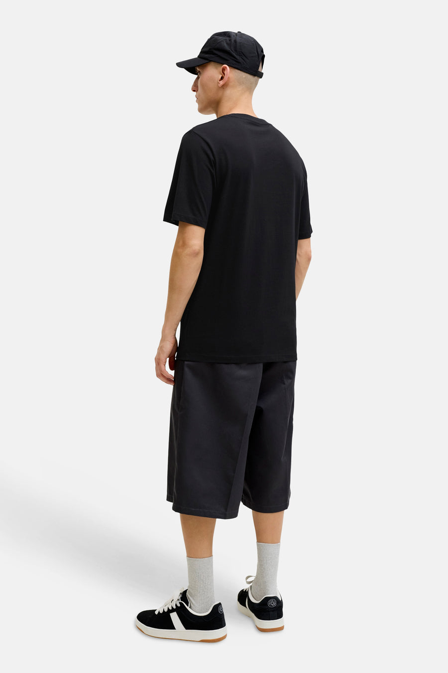 T-shirt noir de JACK & JONES, porté de dos avec un short, une casquette, des chaussettes grises et des baskets.