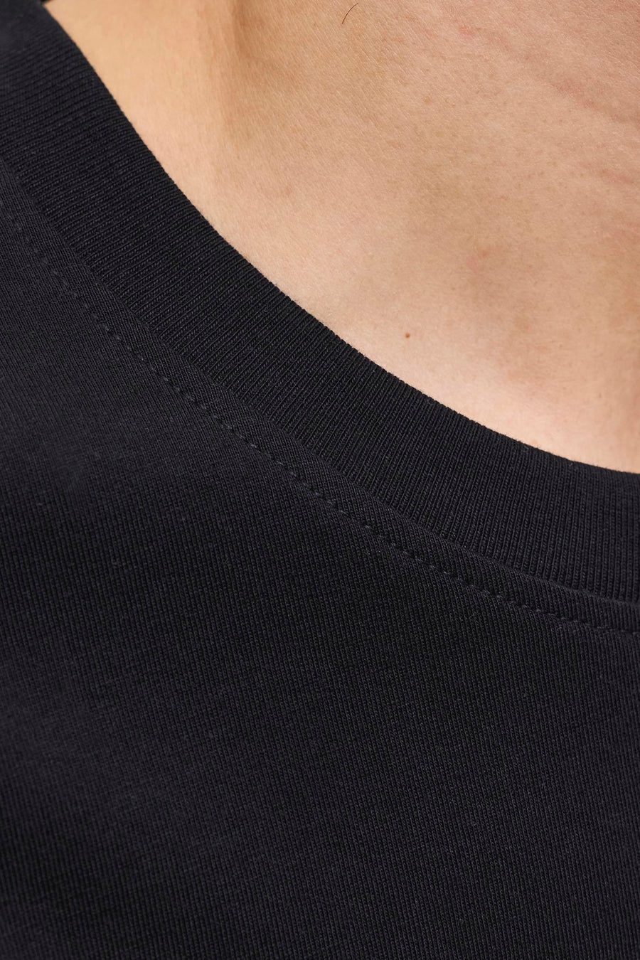 Gros plan sur le t-shirt noir de JACK & JONES avec col côtelé et couture visible sur peau claire.