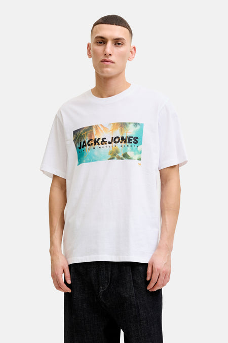 T-shirt blanc de JACK & JONES avec un imprimé tropical de palmiers et le logo sur le devant, porté avec un jean foncé.