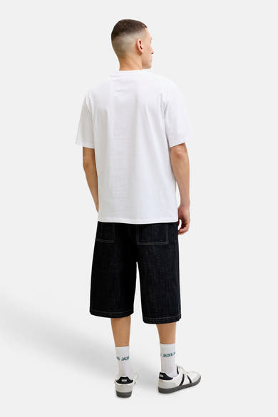 T-shirt blanc à manches courtes de JACK & JONES, porté de dos avec un short en jean foncé à coutures contrastantes et des baskets.