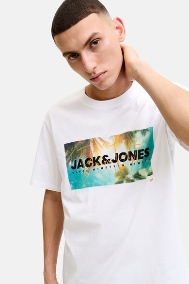T-shirt blanc à manches courtes de JACK & JONES avec un imprimé graphique palmiers et logo, porté par un homme.