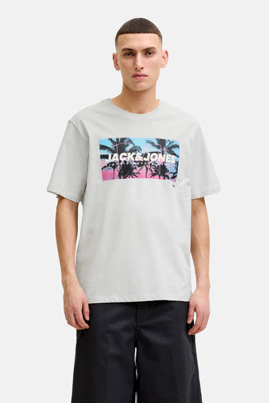 T-shirt blanc de JACK & JONES avec grand imprimé dégradé bleu-rose, palmiers et logo, porté avec un short noir.