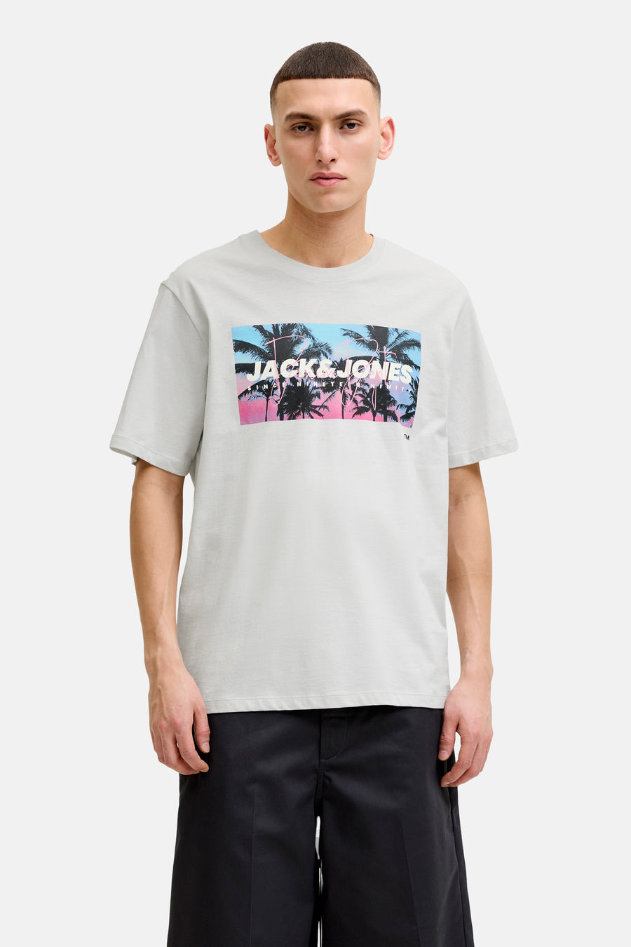 T-shirt blanc de JACK & JONES avec grand imprimé dégradé bleu-rose, palmiers et logo, porté avec un short noir.