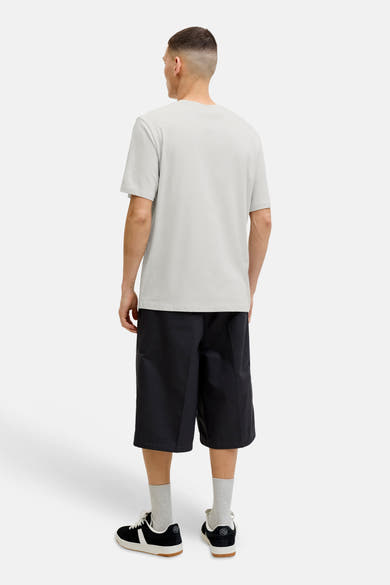 T-shirt blanc à manches courtes de JACK & JONES, porté de dos avec un short noir et des baskets.