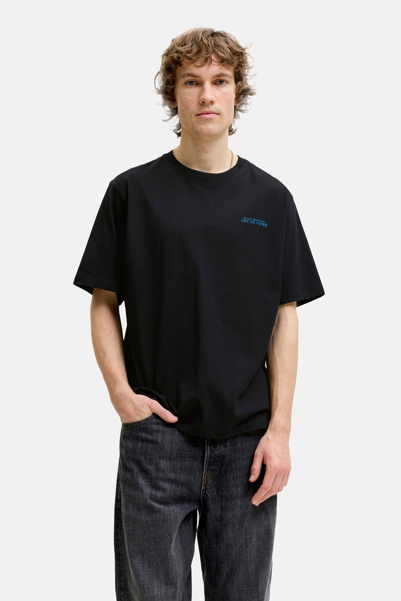 Black short-sleeve t-shirt with blue embroidered text on chest, worn by model in front view with dark jeans.