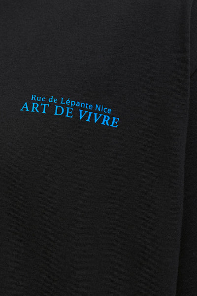 Black short-sleeve t-shirt with blue embroidered text "Rue de Lépante Nice ART DE VIVRE" on chest, close-up view