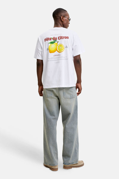 White short-sleeve T-shirt with lemon graphic and "Fête du Citron" text, back view, worn with light blue jeans and tan shoes