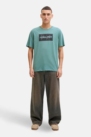 T-shirt à manches courtes bleu, de JACK & JONES, avec un imprimé graphique sur le devant, porté avec un pantalon ample.
