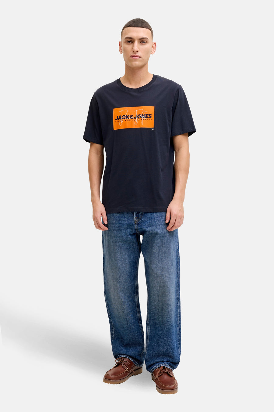 T-shirt bleu à manches courtes de JACK & JONES, avec un logo graphique orange sur le devant, porté avec un jean ample.
