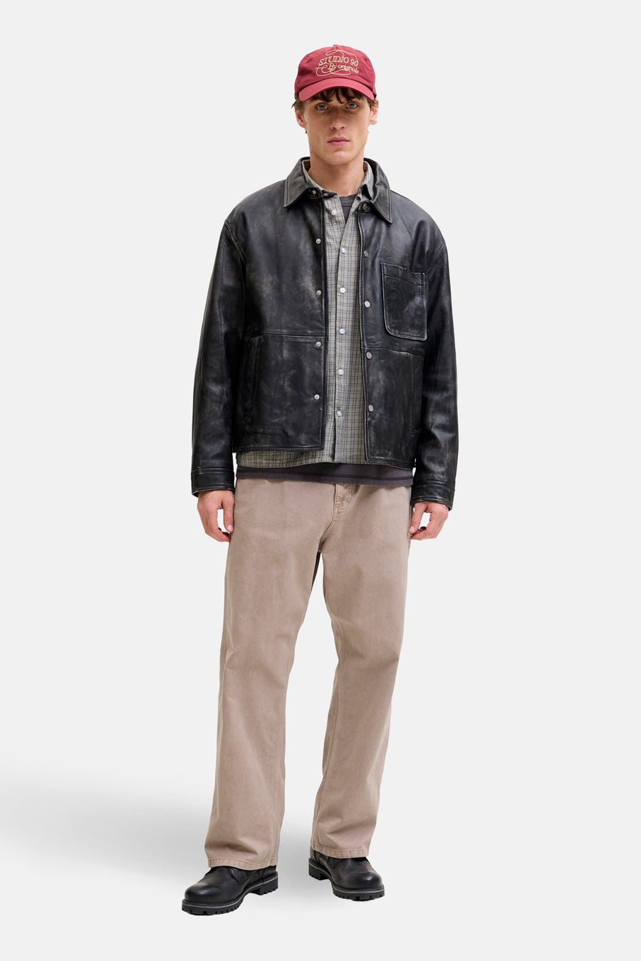 Beige broek van JACK & JONES JEANS INTELLIGENCE, gedragen met een zwart leren jasje en een bordeauxrode pet.