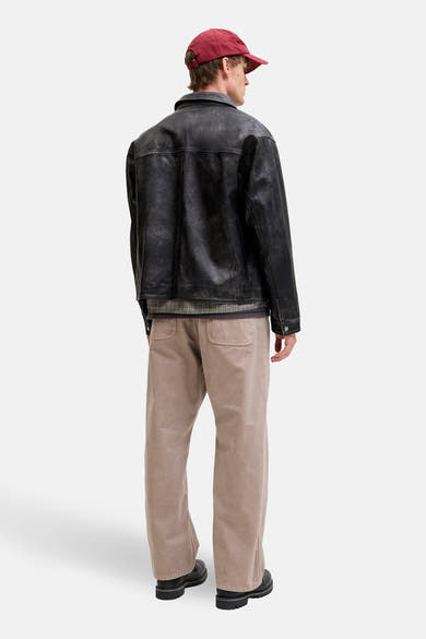 Beige broek van JACK & JONES JEANS INTELLIGENCE, gedragen met een leren jasje en een bordeauxrode pet.