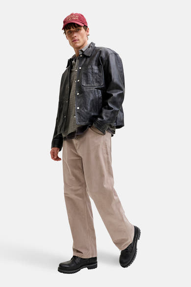 Beige broek JACK & JONES JEANS INTELLIGENCE, gedragen met een zwart leren jasje en een bordeauxrode pet.