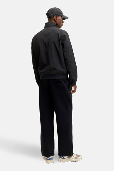 Zwarte regenjas van ORIGINALS BY JACK & JONES, gedragen met een zwarte broek en sportschoenen.
