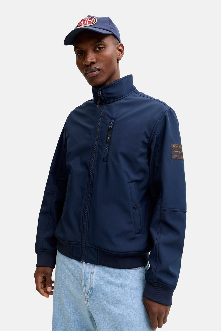 Veste de pluie bleue par ORIGINALS BY JACK & JONES, avec fermeture éclair, porté avec un jean clair et une casquette bleu marine.