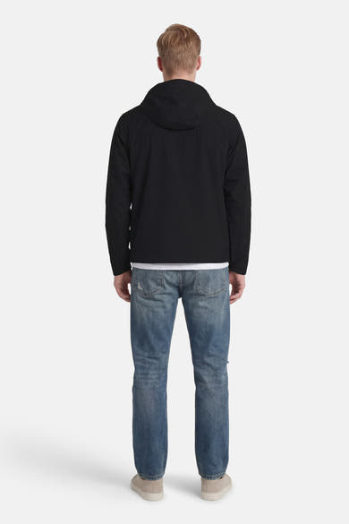 Korte zwarte jas van JACK & JONES, met capuchon, gedragen met een spijkerbroek en beige sneakers, van achteren gezien.