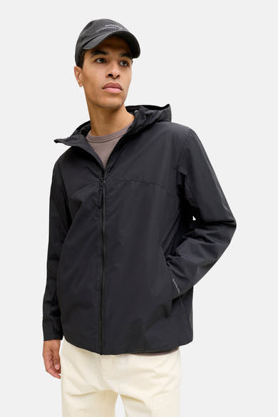 Kort zwart jack van JACK & JONES, gedragen met een lichte hoed en broek.