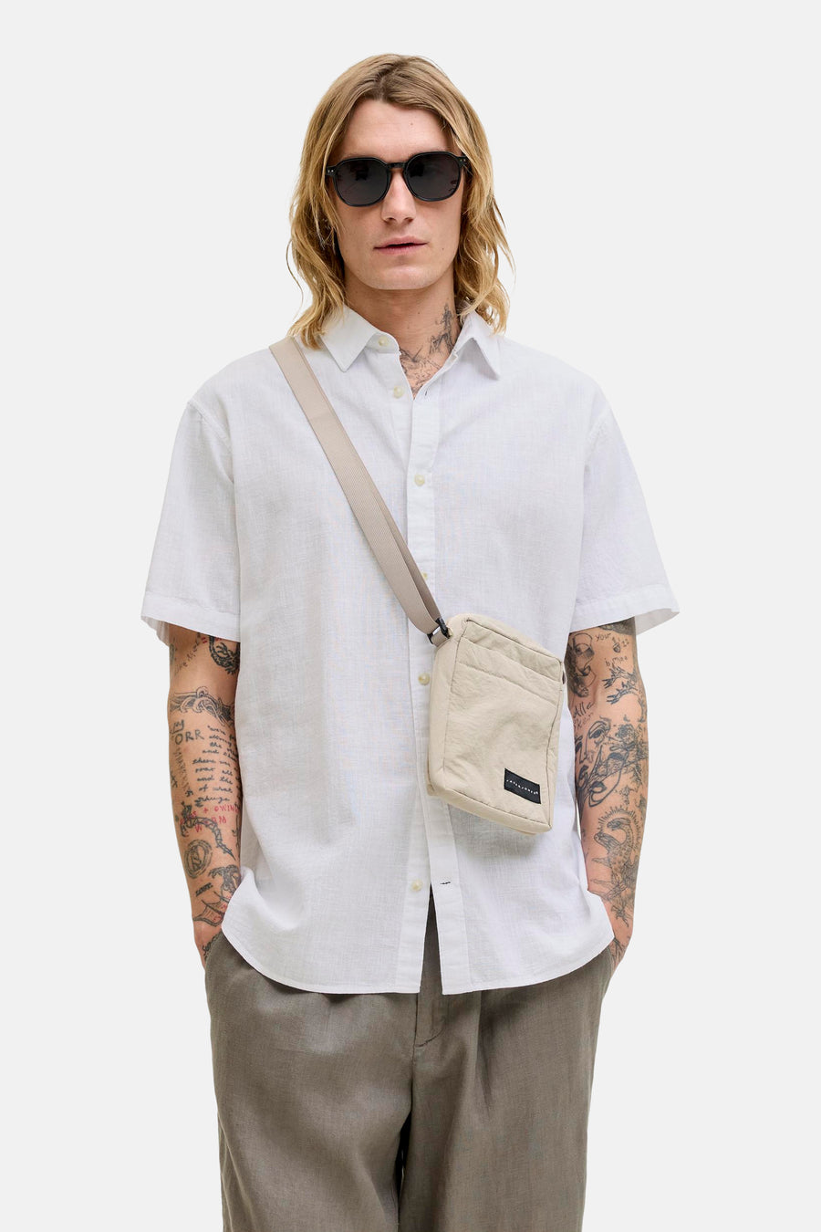 Chemise blanche à manches courtes de JACK & JONES, portée avec un sac bandoulière et un pantalon gris.
