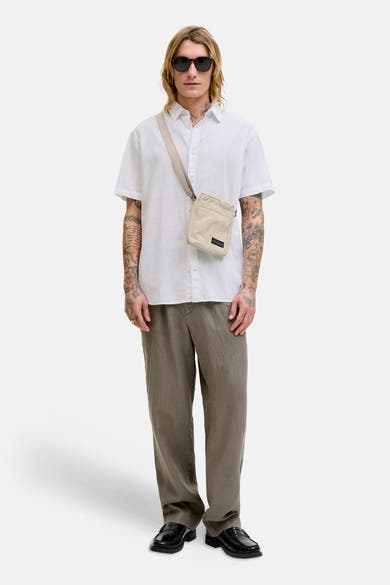 Chemise blanche à manches courtes de JACK & JONES, portée avec un sac bandoulière et un pantalon olive en lin.