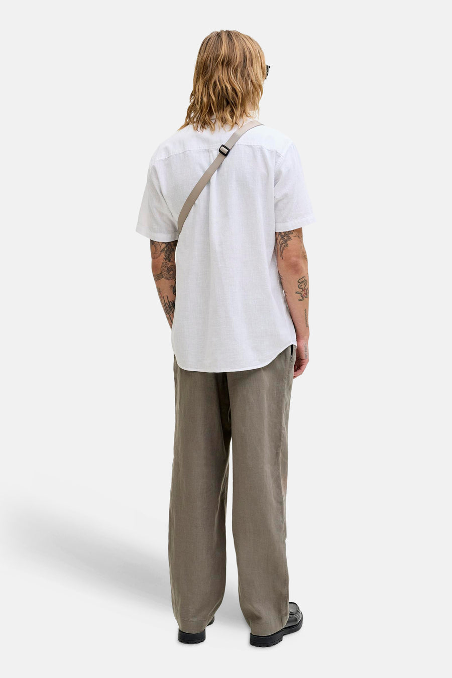 Chemise blanche à manches courtes de JACK & JONES avec une bandoulière grise et des tatouages sur les bras.