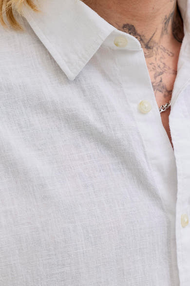 Chemise blanche à manches courtes de JACK & JONES, avec une texture en lin visible et des boutons apparents.