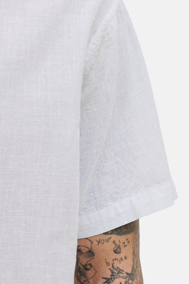 Chemise blanche à manches courtes de JACK & JONES, texture de lin visible et tatouages sur le bras.