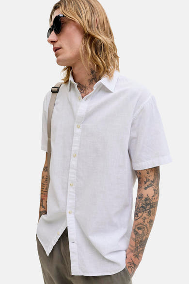 Chemise blanche à manches courtes de JACK & JONES, portée ouverte, avec motifs de tatouages sur le bras.