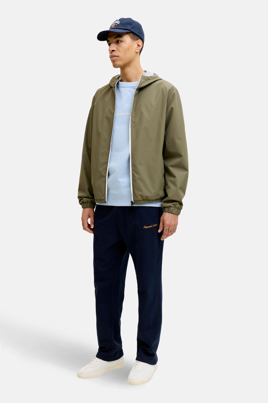 Veste courte verte par ORIGINALS BY JACK & JONES, portée avec un t-shirt bleu clair, un pantalon de survêtement et une casquette.