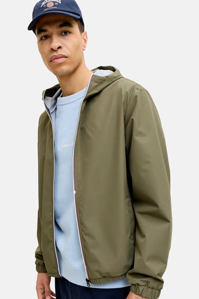 Kort olijfgroen jack van ORIGINALS BY JACK & JONES, met capuchon en ritssluiting, gedragen met een lichtblauwe trui en een marineblauwe pet.