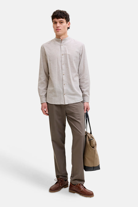 Chemise à manches longues beige de JACK & JONES, col mao, portée par un homme avec un pantalon marron, des chaussures bateau et un sac en toile.