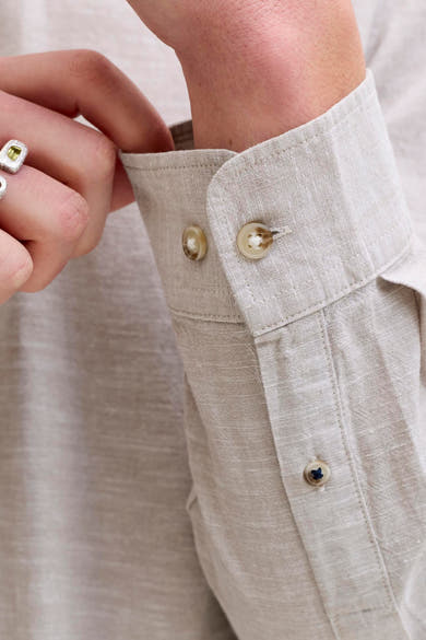 Chemise à manches longues beige de JACK & JONES en lin texturé, manchette boutonnée avec boutons clairs et petit bouton à fil foncé, une main ajustant le poignet.