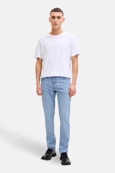 Jean slim en denim bleu clair de JACK & JONES JEANS INTELLIGENCE, porté avec un t-shirt blanc et des chaussures noires.
